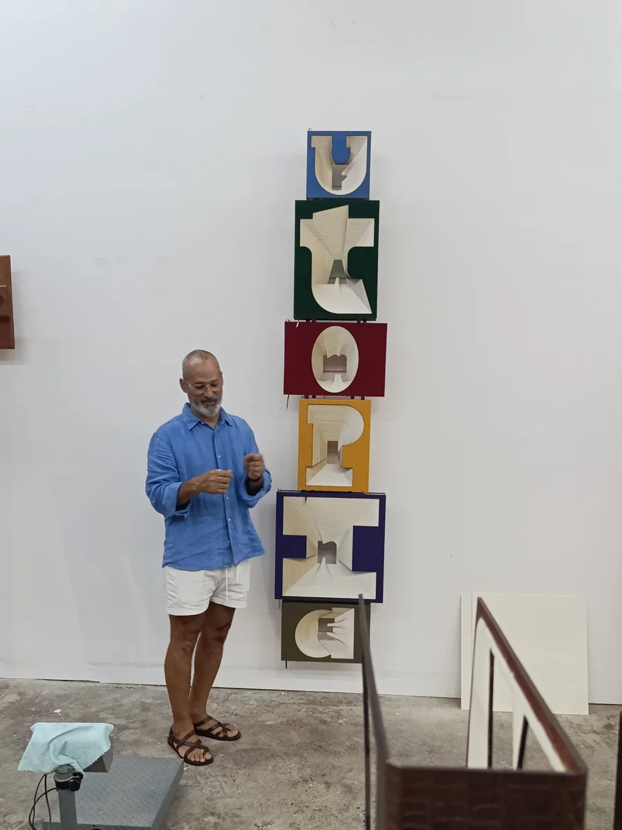 Marcos Castillo next to his vertical polychrome letter sculpture in his studio