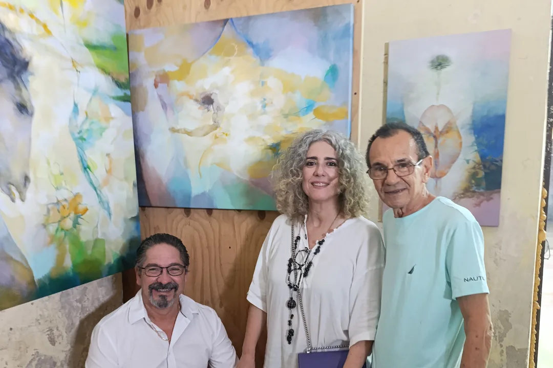 Two men and a woman posing in front of large abstract paintings in an artist's studio.