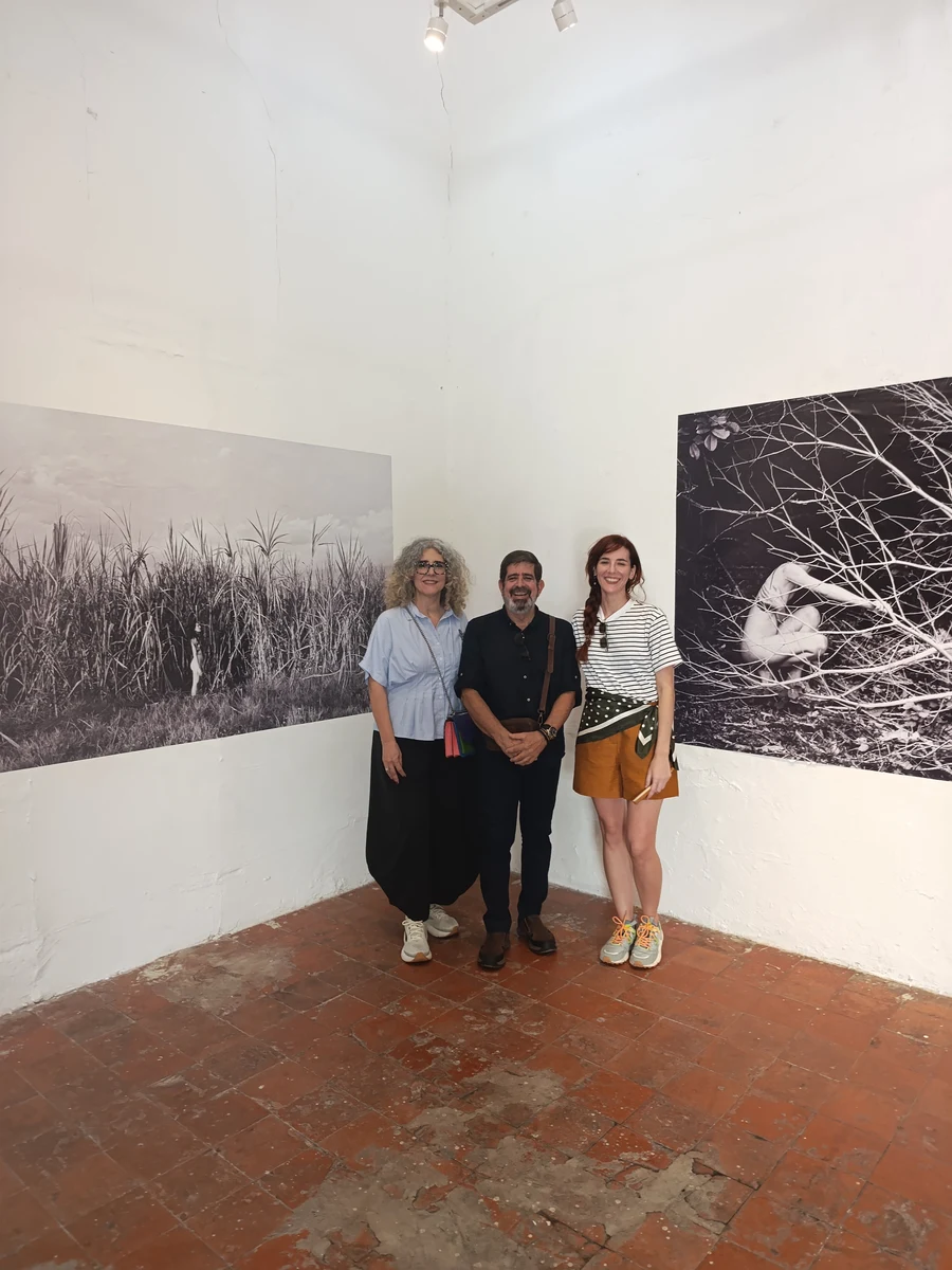 Ivonne Ferrer, Leonardo Rodríguez and Laura Capote posing between two black-and-white photographic works at the exhibition in Mérida.