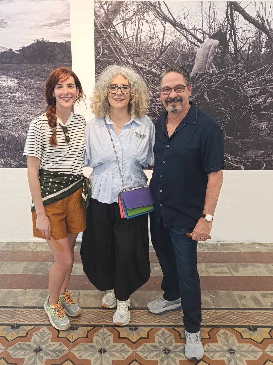 Laura Capote with Ivonne Ferrer and Leonardo Rodríguez posing before her large-format photographs at the Mérida Visual Arts Center.