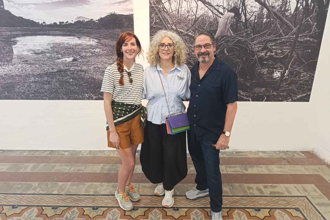 Laura Capote, Ivonne Ferrer and Leonardo Rodríguez posing in front of large black-and-white photographs at Laura Capote's exhibition in Mérida.