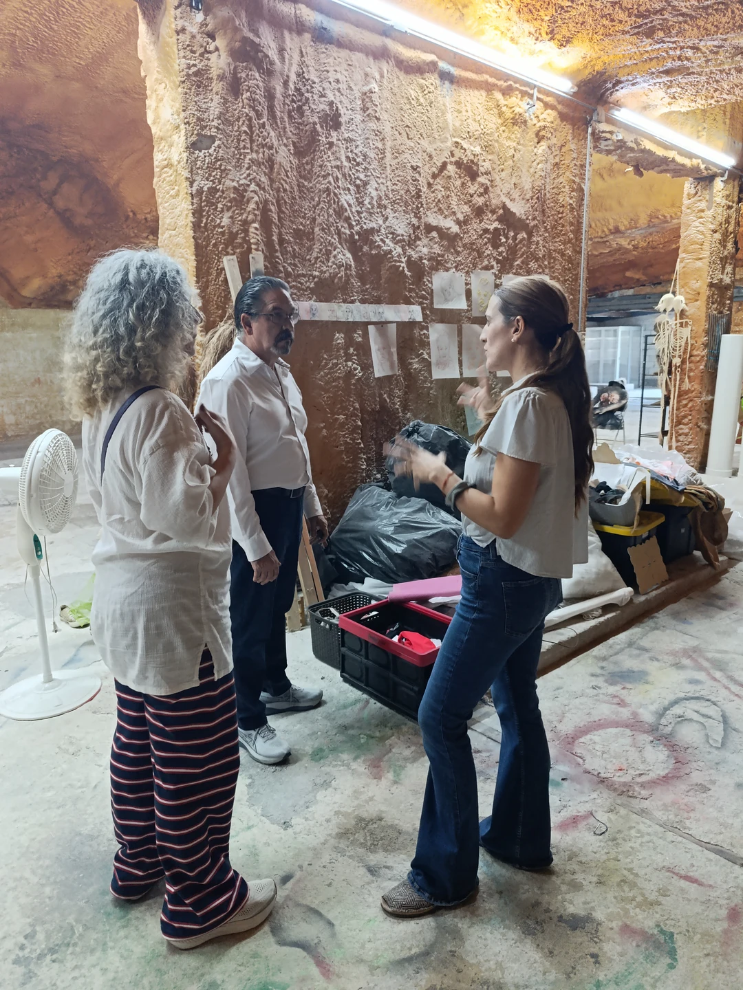 Claribel Calderius, Leonardo Rodríguez and Ivonne Ferrer looking at drawings pinned to the textured wall of the studio.