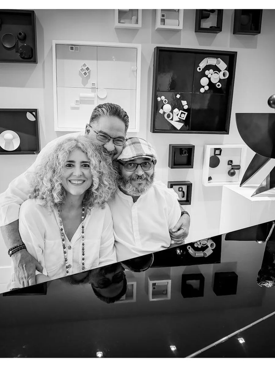 Ivonne Ferrer, Gary A. Añuez and Leonardo Rodríguez posing together in the studio among geometric wall sculptures, in black and white