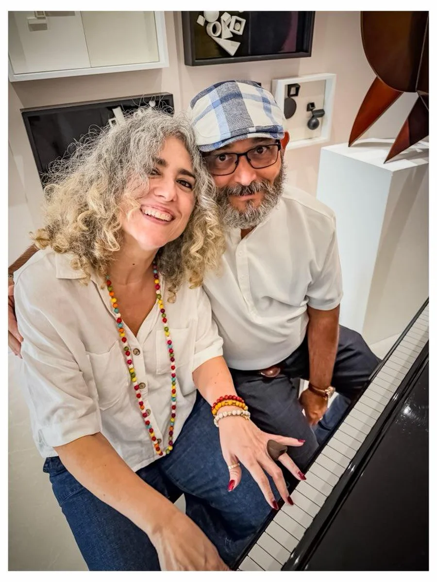 Ivonne Ferrer and Gary A. Añuez seated together at a piano in the artist's studio in Florida
