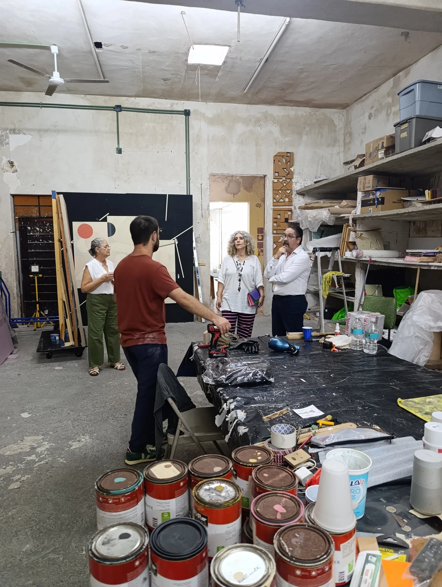 Four people in the studio looking at geometric abstract works on the walls, with paint cans and tools around.