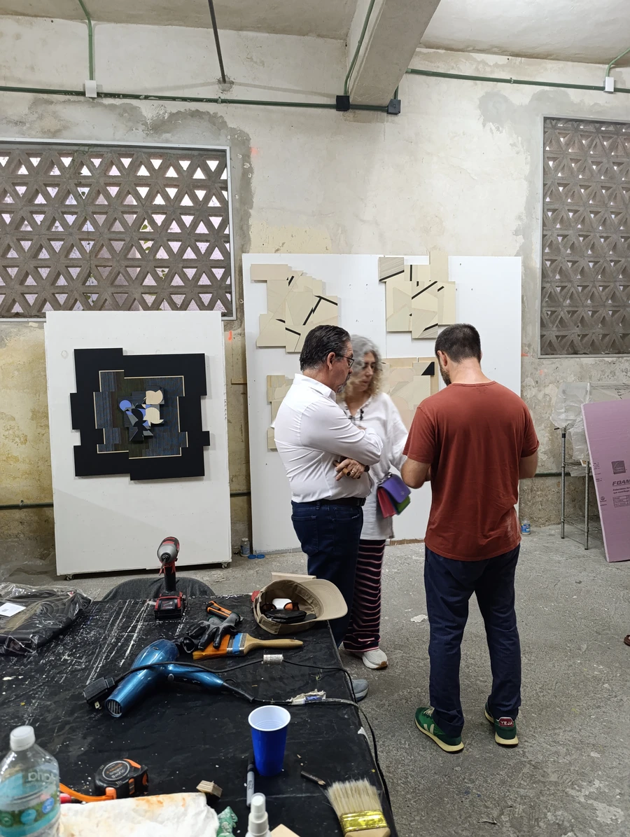 Three people examining geometric abstract reliefs mounted on white panels in the studio.