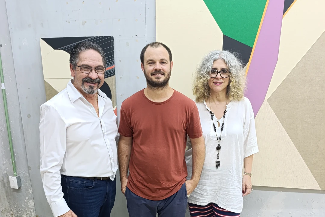 Leonardo Rodríguez, Ernesto García Sánchez and Ivonne Ferrer posing in the artist's studio in Mérida, in front of colorful geometric abstract paintings.