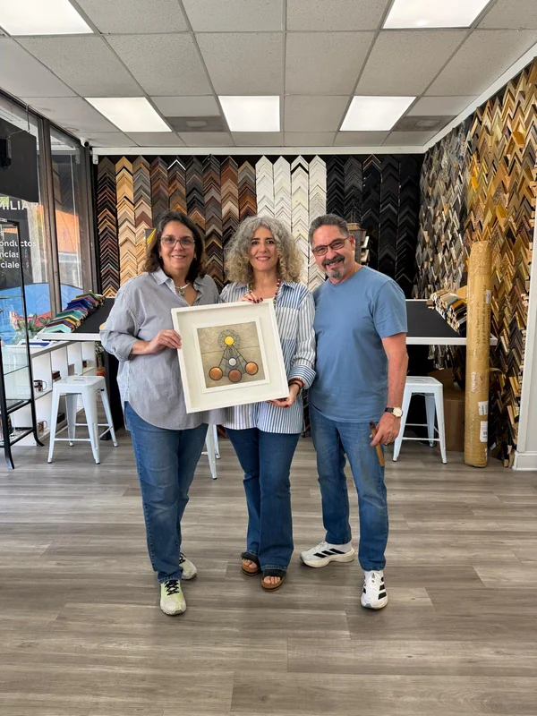 Three people posing with the framed artwork inside the Frame on Wheels shop