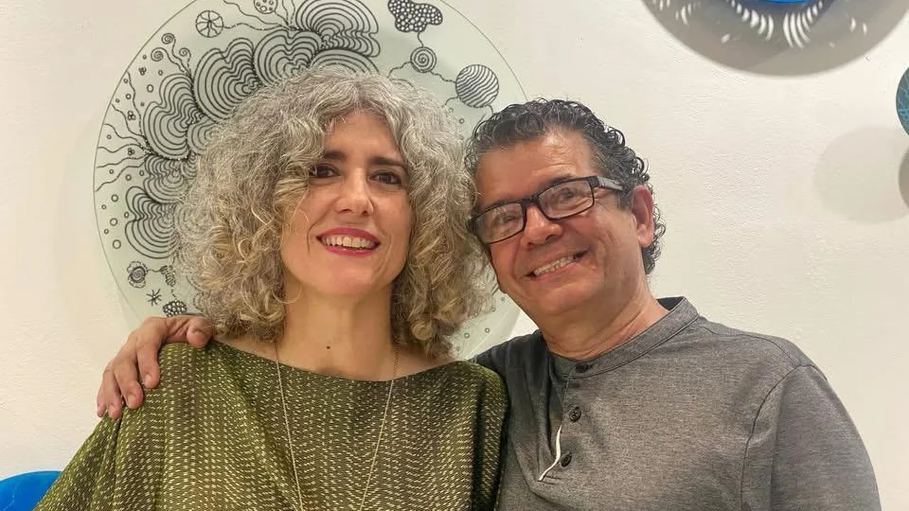 Two guests smiling in front of a circular artwork at the opening of Beauty as Protest.