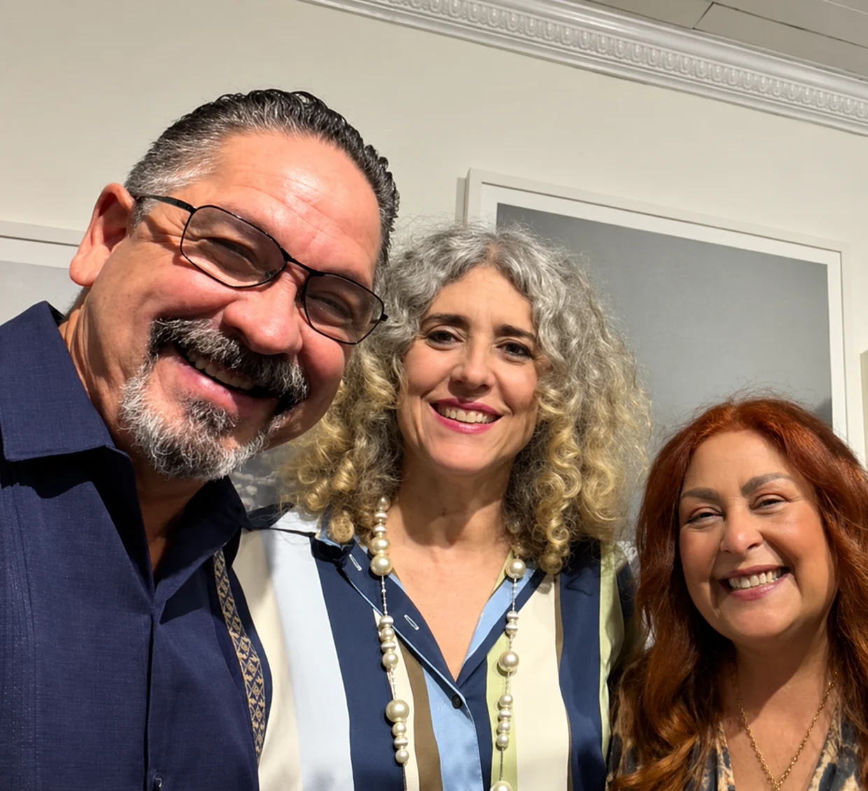 Three people smiling together in a gallery.