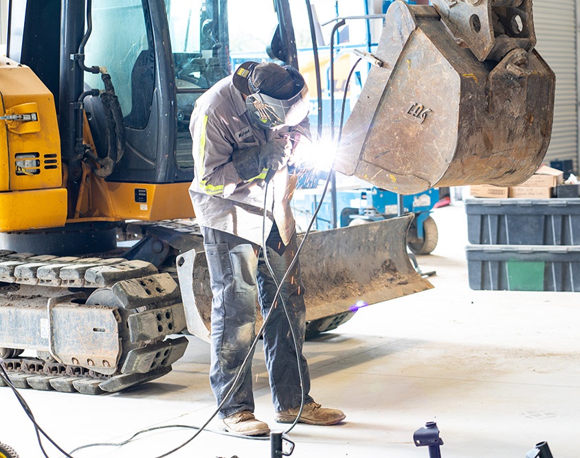 A tech performing some reparative welding on an excavator bucket