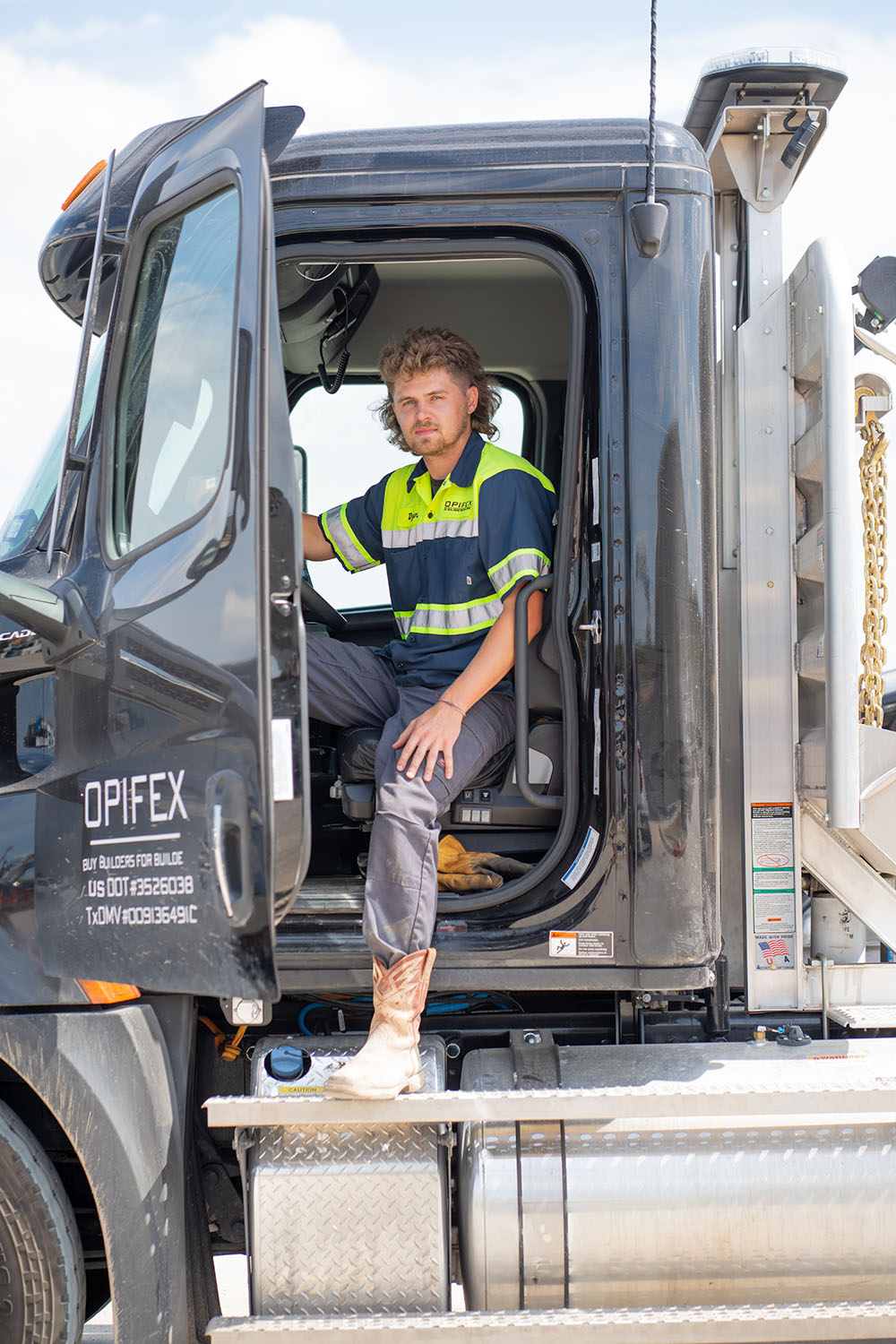 A driver is sitting in a delivery vehicle with the door open, looking at the camera
