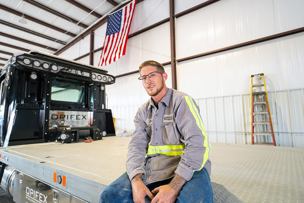 A worker is sitting on the back of a delivery truck, looking at the camera