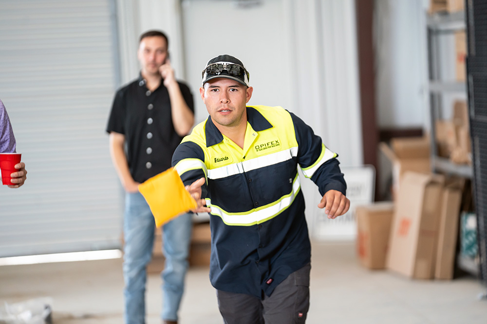 Some of our employees are playing cornhole at the shop. One is throwing his bag with a very focused expression.