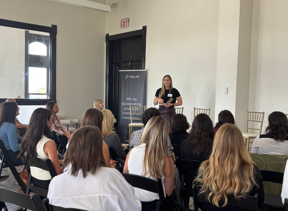 Jennifer Daugherty from Zaelab delivers opening remarks to the audience at the Women in B2B Thought Leadership Collective, with Zaelab and Shopify event banners behind her.