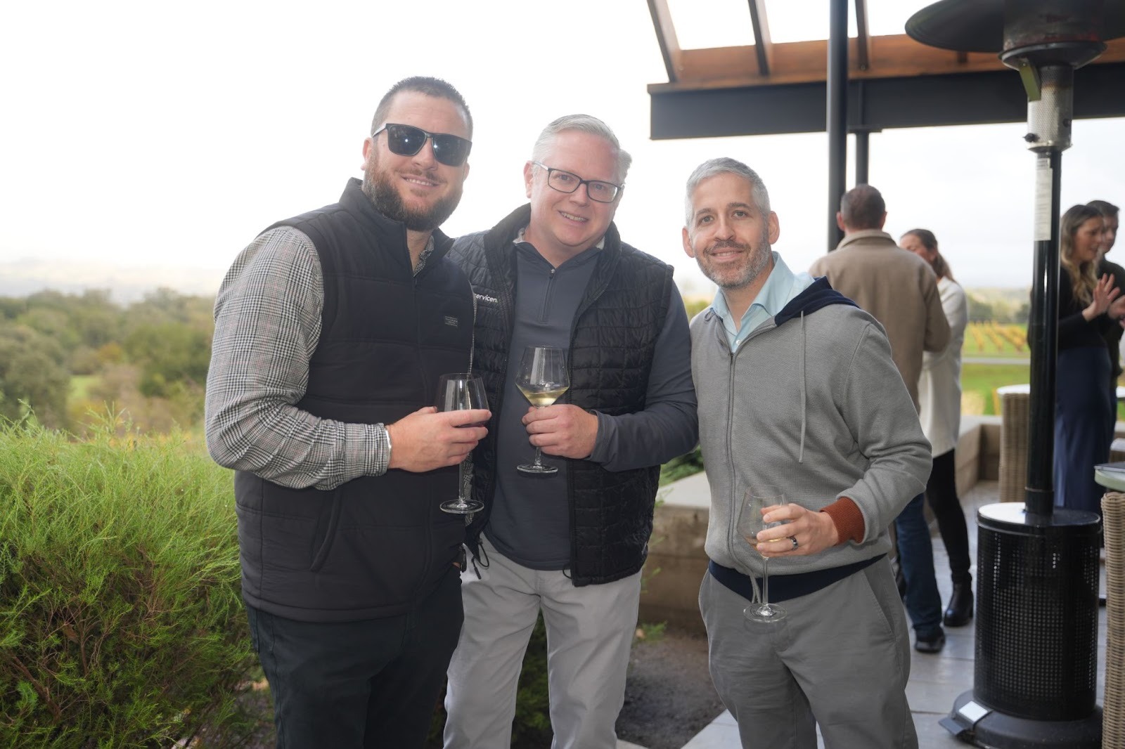 Three attendees smiling for a photo while holding wine glasses on a patio at the Better Together 2025 event in Sonoma, hosted by Zaelab in partnership with ServiceNow and Shopify.