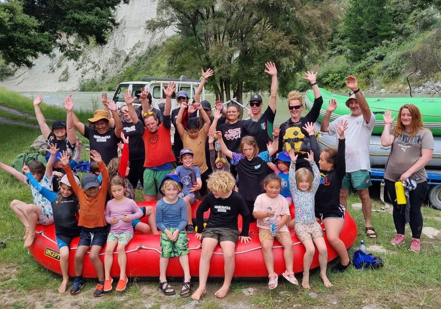 a group of local school kids and parents sitting on a raft waving at the take out of the rangitikei river at mangaweka