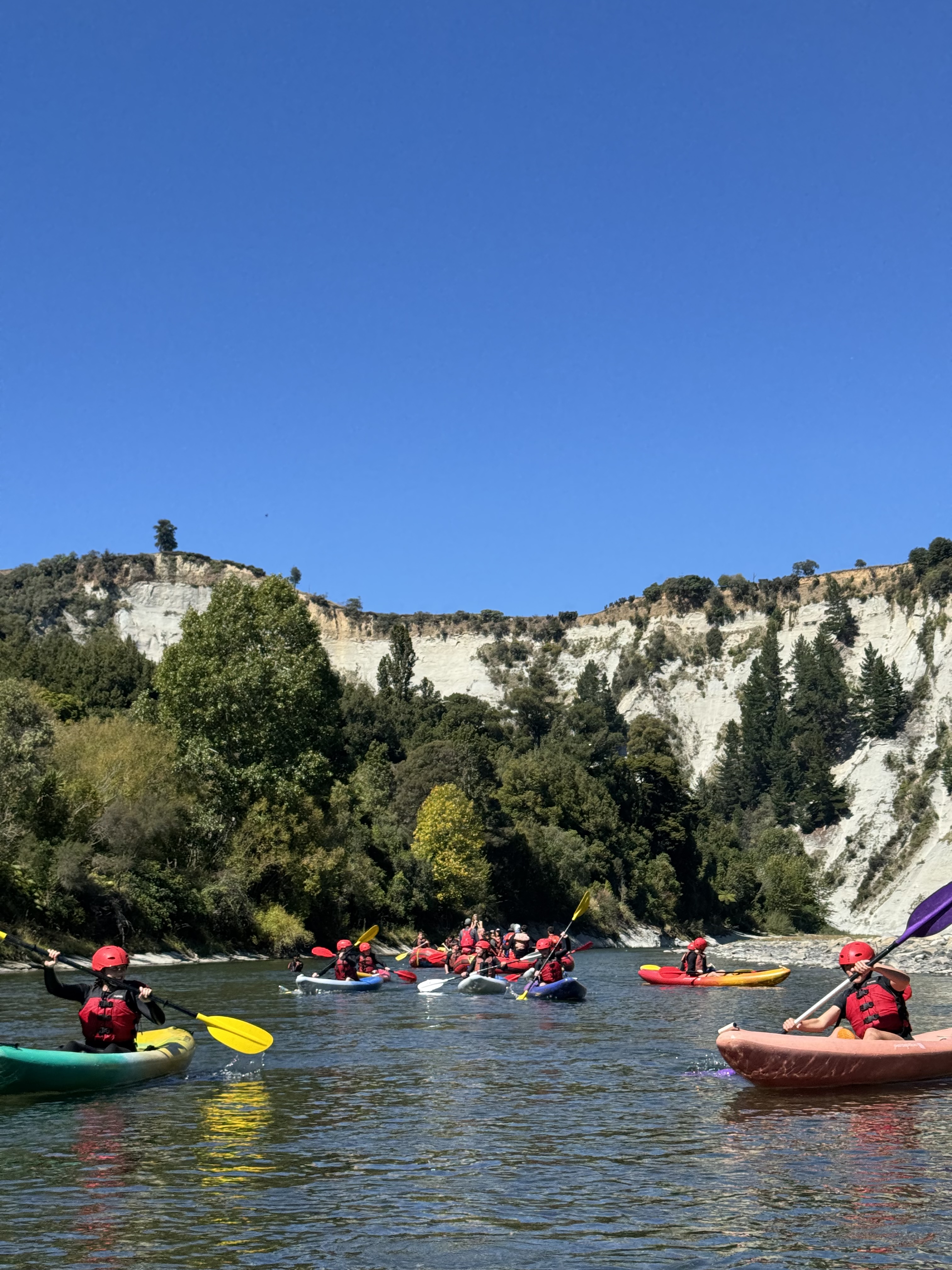 a group of school students swimming and playing in the rangitikei river at awastone mangaweka, a mix of rafts and kayaks are floating down a calm pool. 