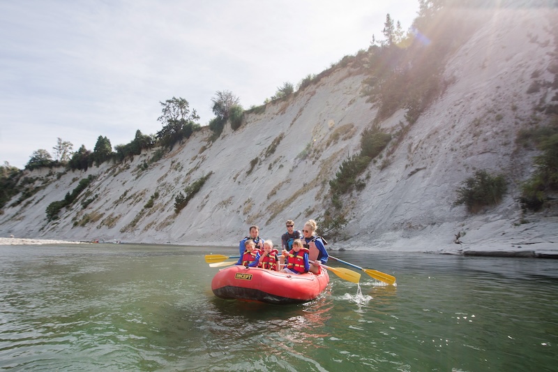 a red raft seats a family of 5 with small children floating in a calm pool underneath tall white papa cliffs in mangaweka new zealand