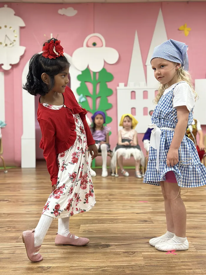 Two young girls in costumes acting and dancing at Children’s Land preschool performance.