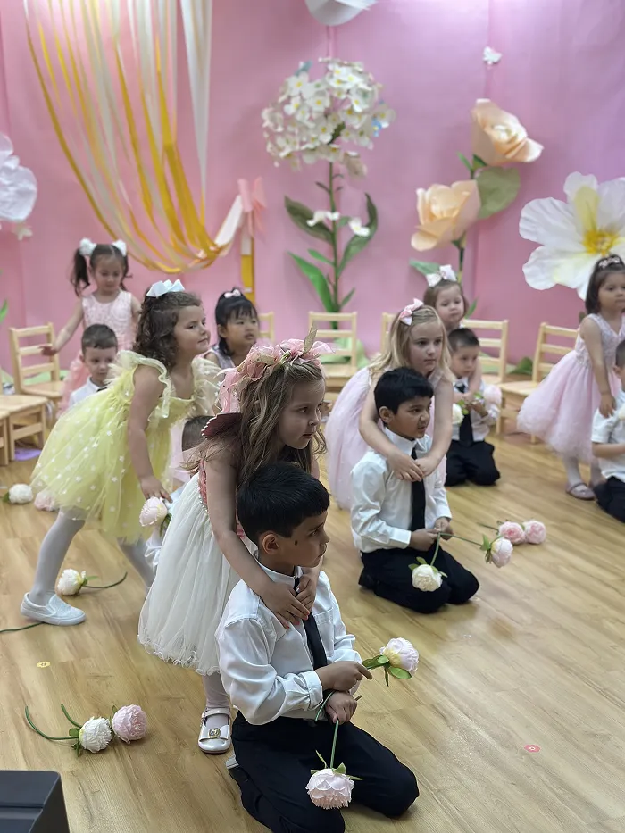 Children in white and gold costumes performing drama and music at Children’s Land preschool.