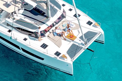Aerial view of a white catamaran with three people relaxing on the deck over clear turquoise water.