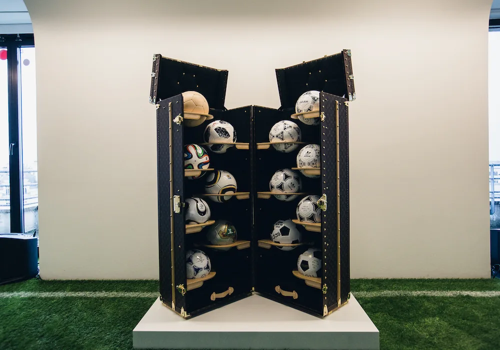 Photo du lancement de la collection Louis Vuitton x FIFA 2018, montrant des ballons dorés et des décorations festives