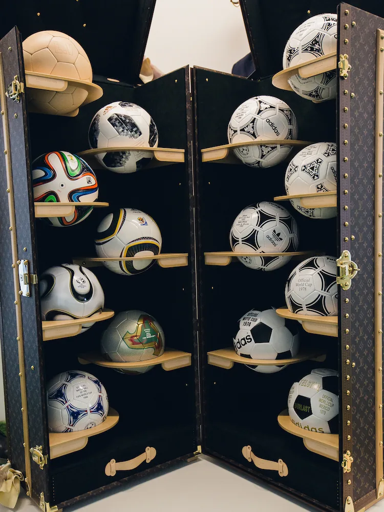 Photo du lancement de la collection Louis Vuitton x FIFA 2018, montrant des ballons dorés et des décorations festives