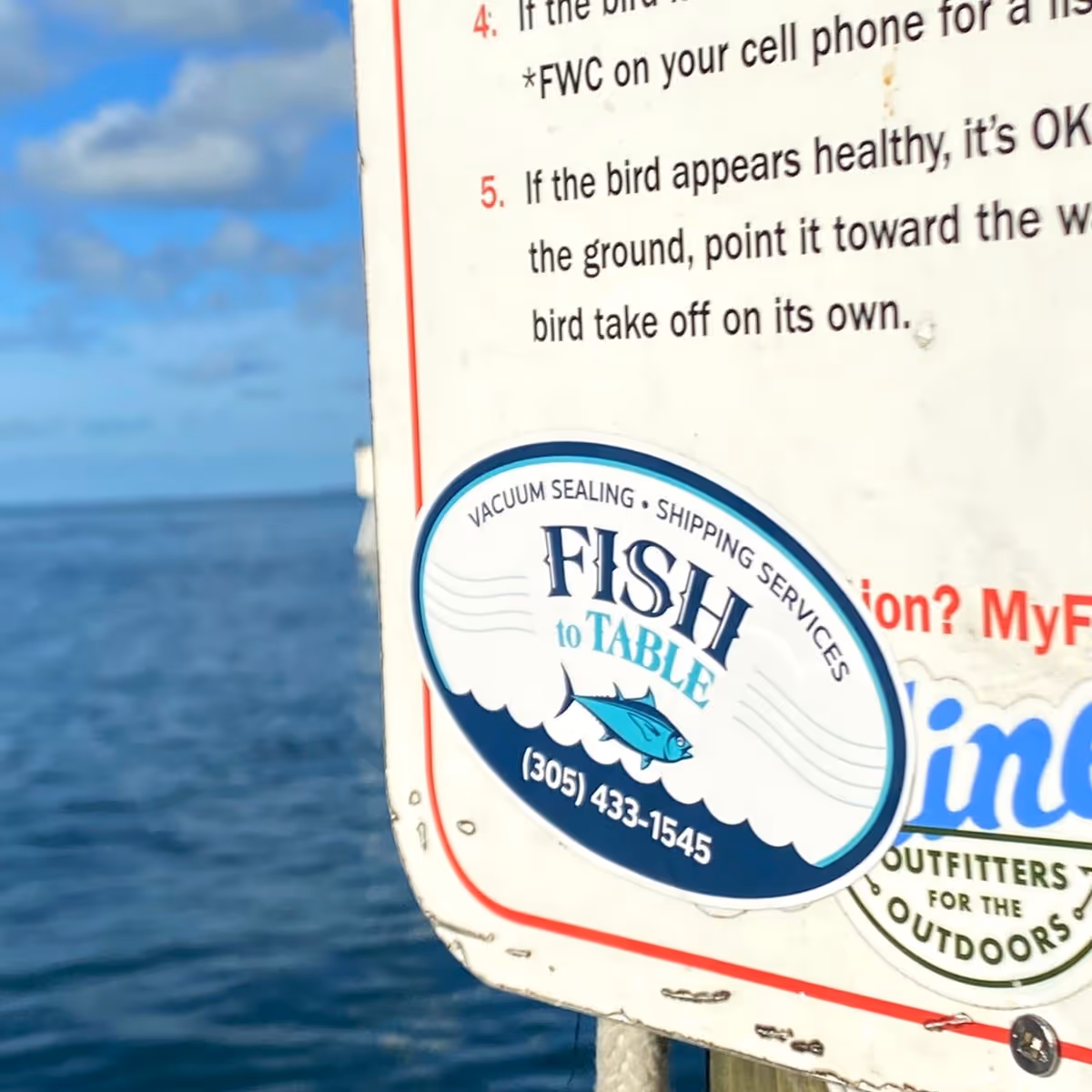 A fish to Table oval sticker on a sign in the Florida Keys with the ocean in the background.