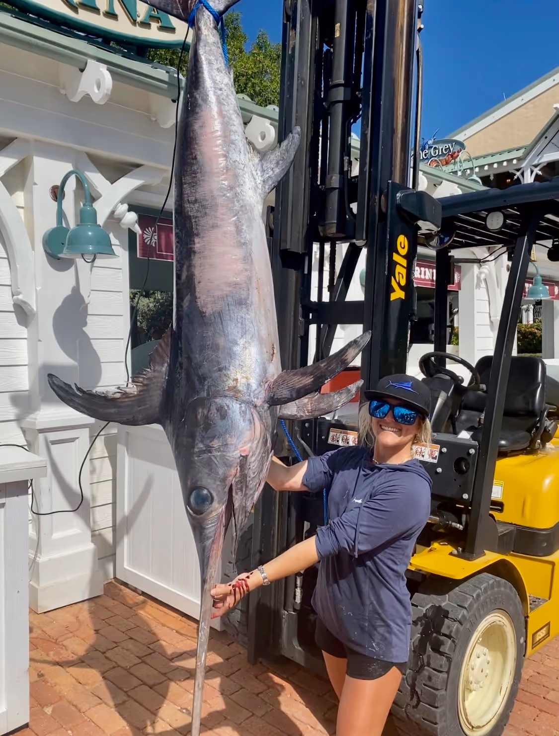 Cailin, owner of Fish to Table stands with a large swordfish that is held up by a forklift on the docks in the Florida Keys.