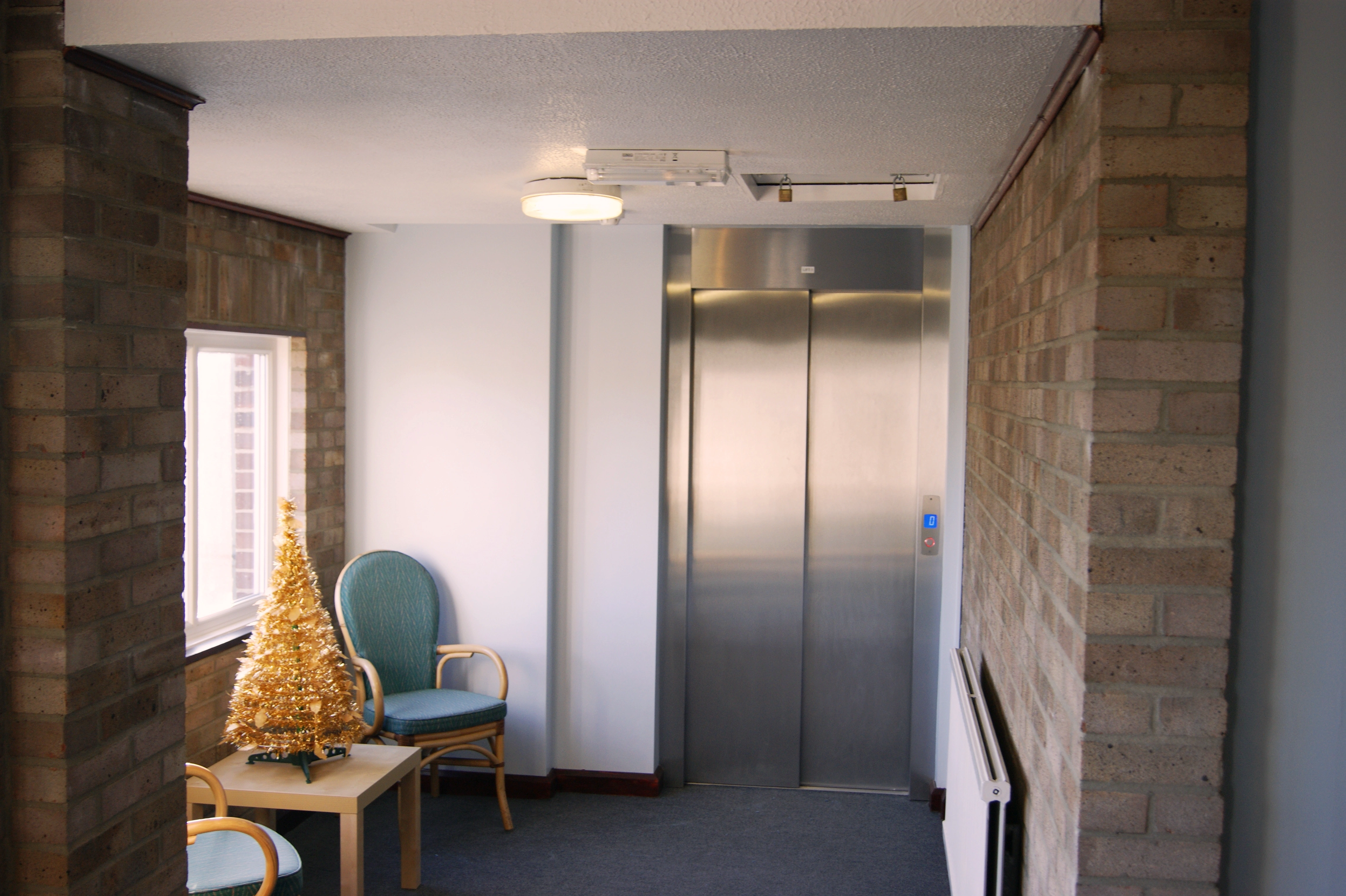 Step lift sited in a rustic brick lift shaft. The wheelchair access lift is finished with fully glazed side panels and black painted steel