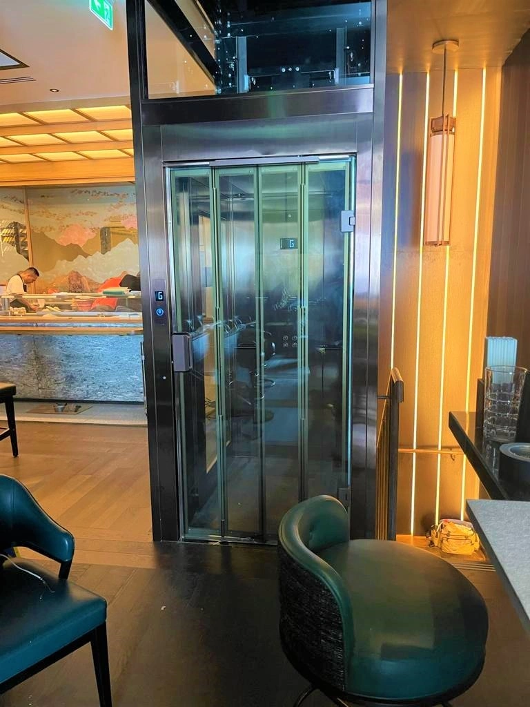 Bespoke DDA access step lift providing wheelchair access between levels in a public building. The step lift has steel painted framework with glass side panels and gate