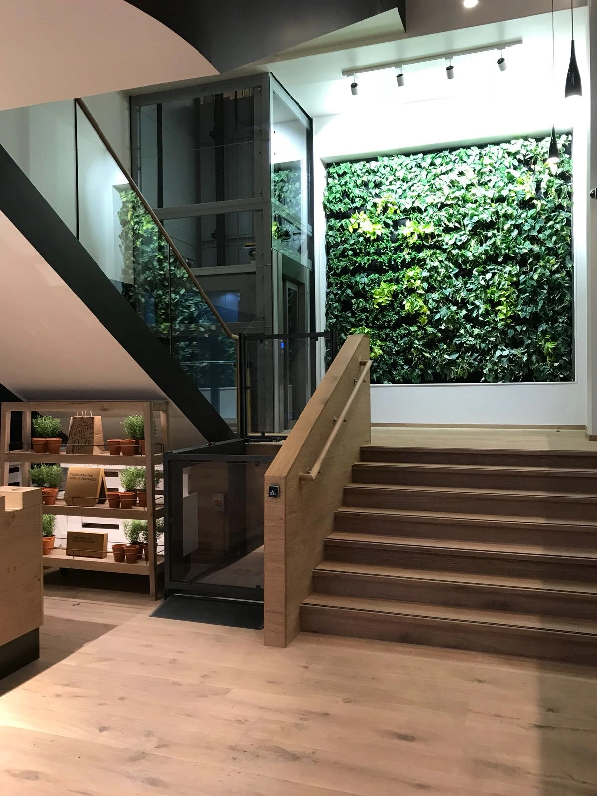 Bespoke DDA access step lift providing wheelchair access between levels in a public building. The step lift has steel painted framework with glass side panels and gate