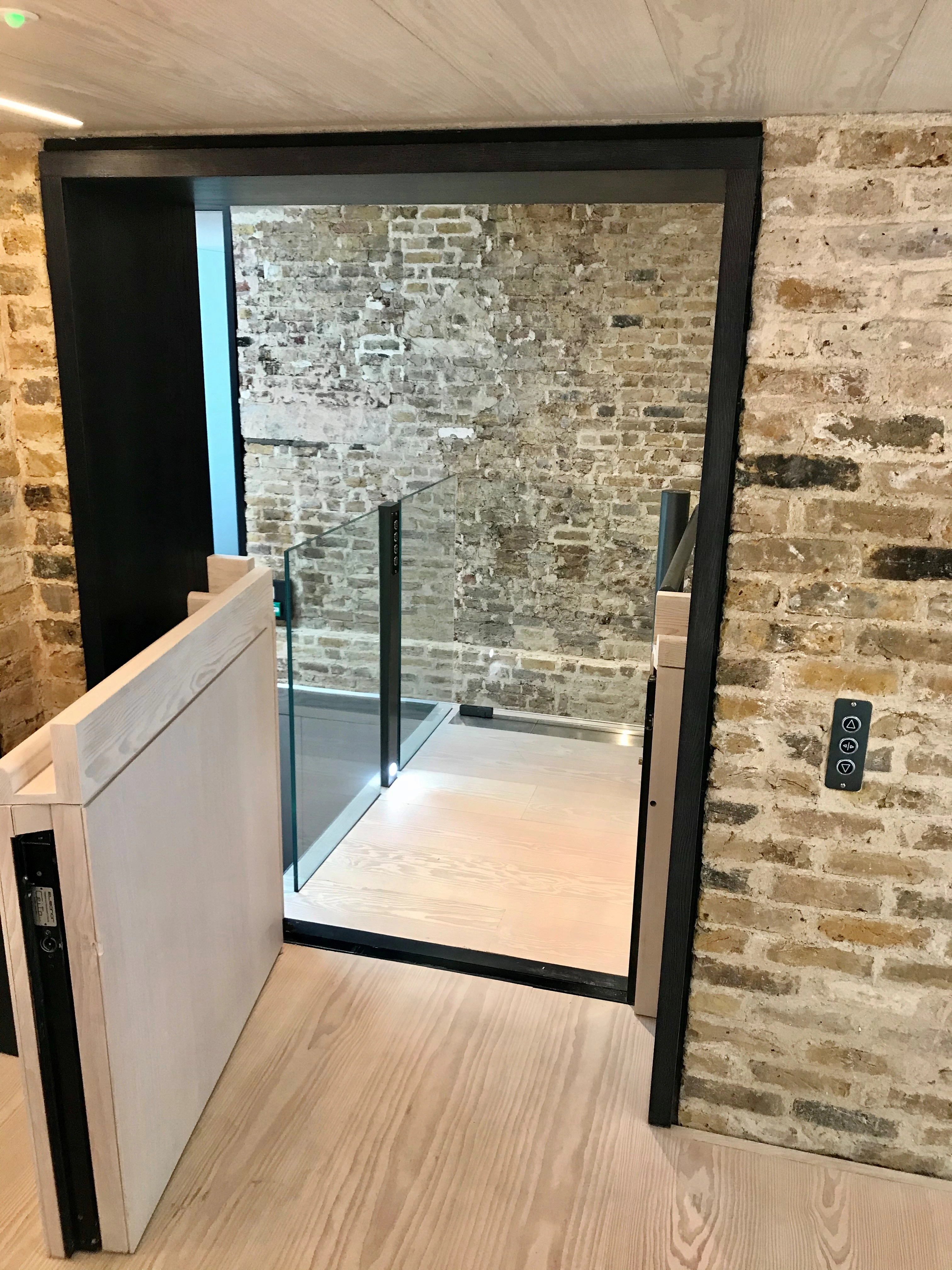 Bespoke DDA access step lift providing wheelchair access between levels in a public building. The step lift has steel painted framework with glass side panels and gate