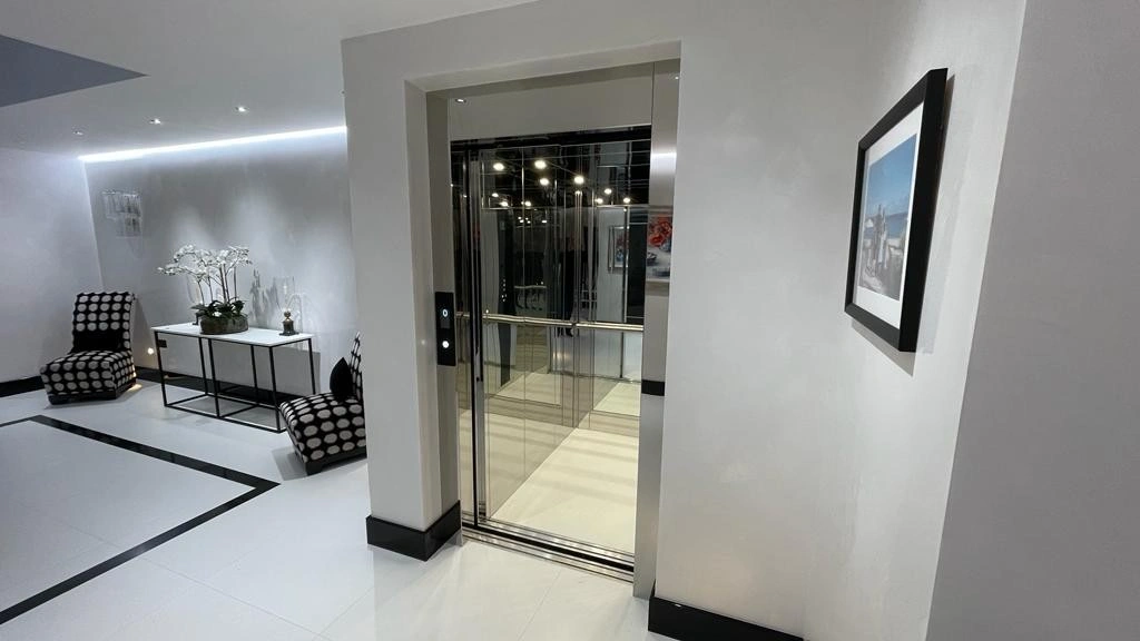 Mirrored Stainless Steel home lift situated next to a curved stainless-steel staircase