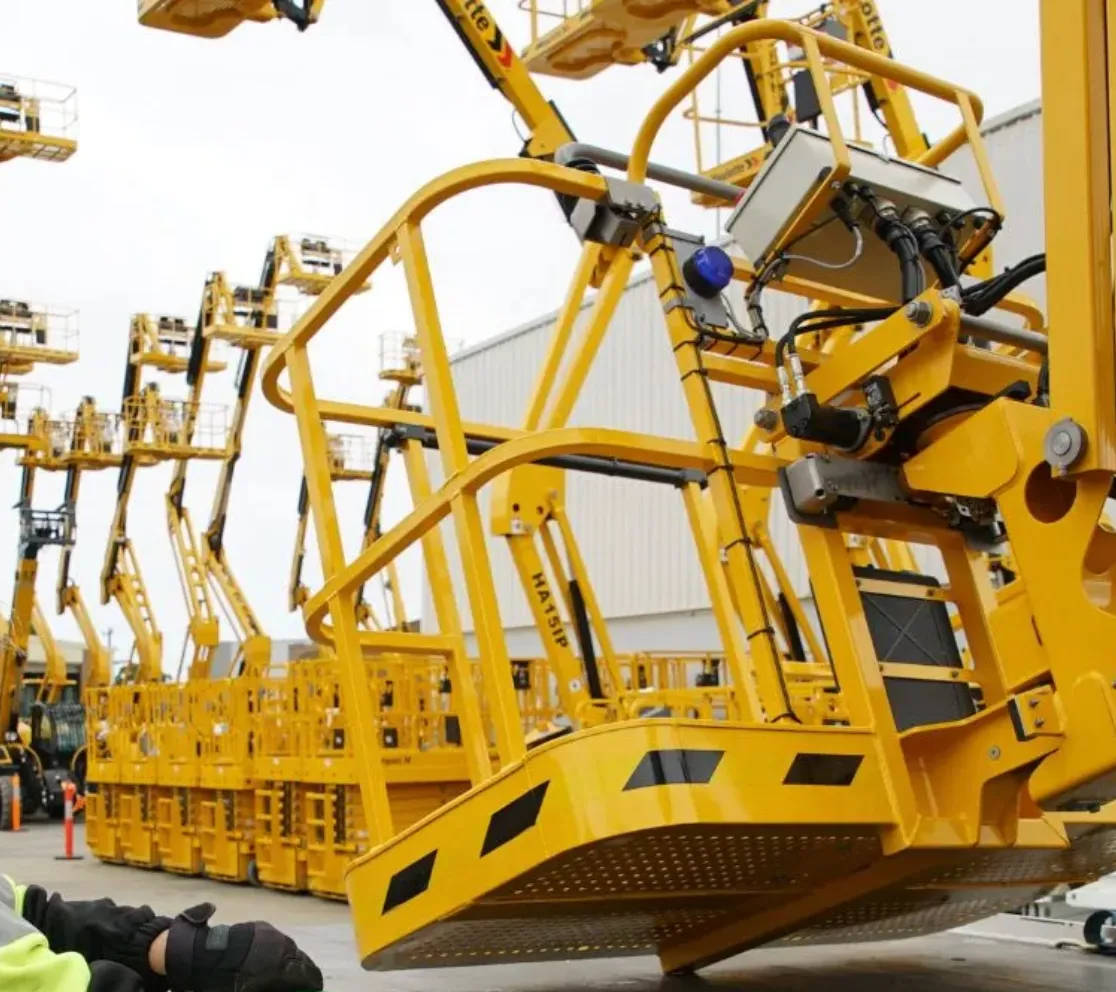 Person in a neon vest secures a yellow lift platform onto a truck with chains.