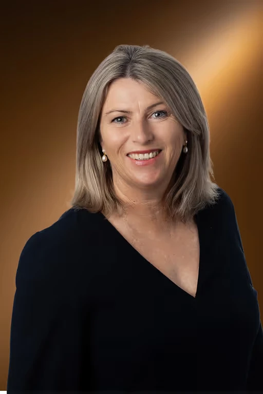 A person with shoulder-length hair and a black top smiles against a brown background.
