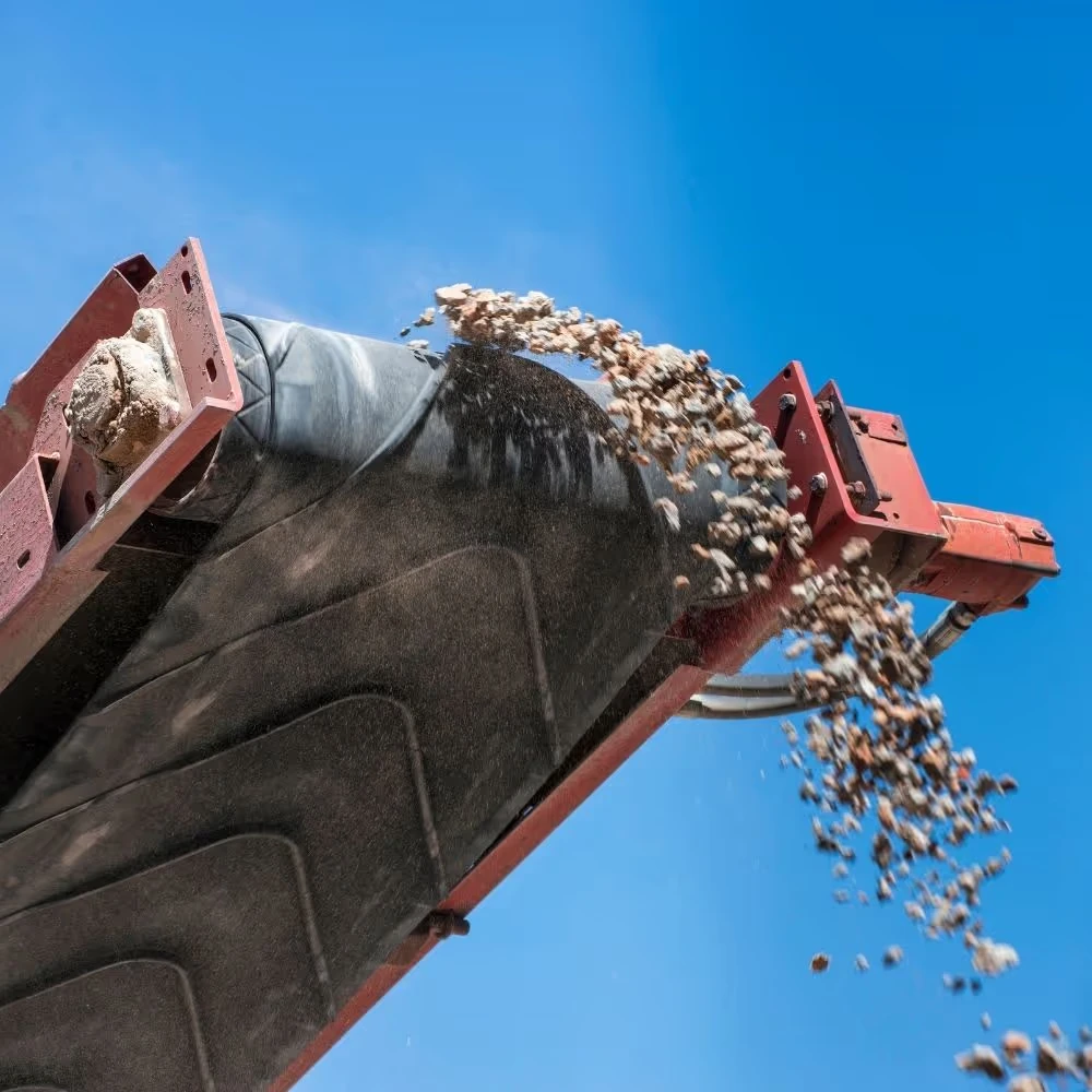 A conveyor belt unloads small rocks under a clear blue sky.