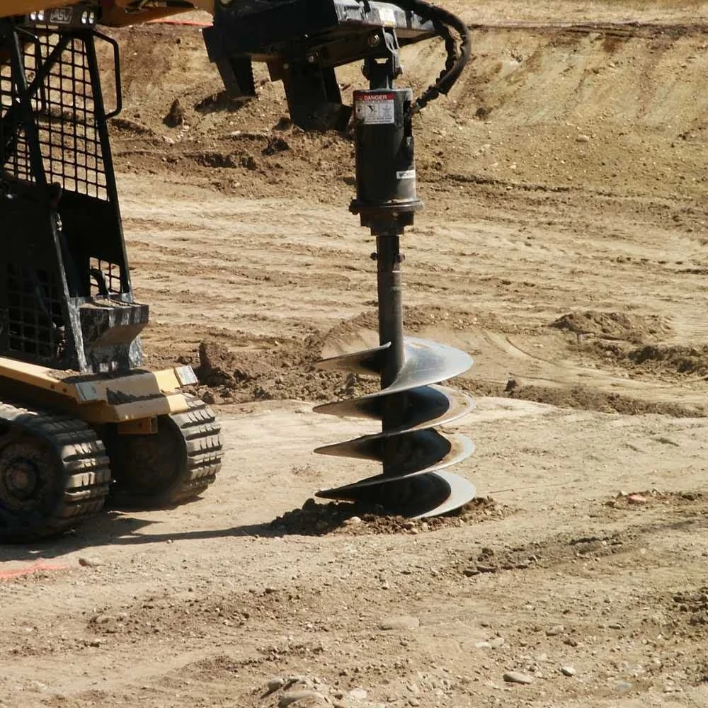 A construction machine is drilling into the ground with a large auger attachment.