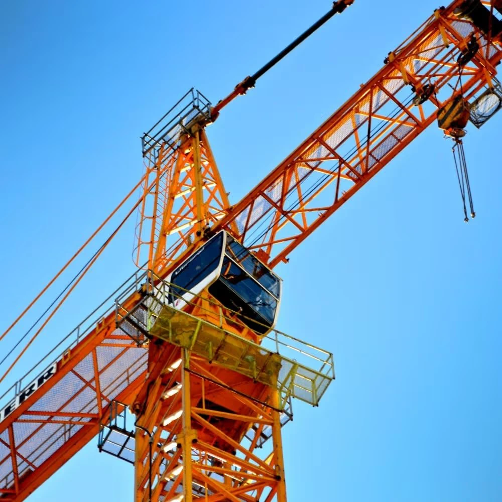 A large orange construction crane with a cabin is set against a clear blue sky.