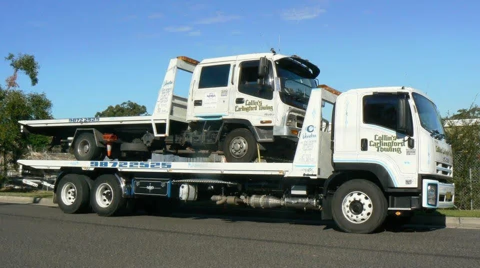 A tow truck is carrying another tow truck on its flatbed along a street.