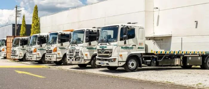 Five white towing trucks are parked in a row on a sunny day.