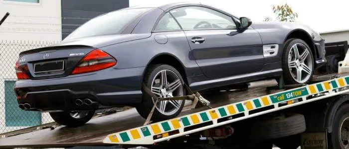 A gray sports car is being towed on a flatbed truck.