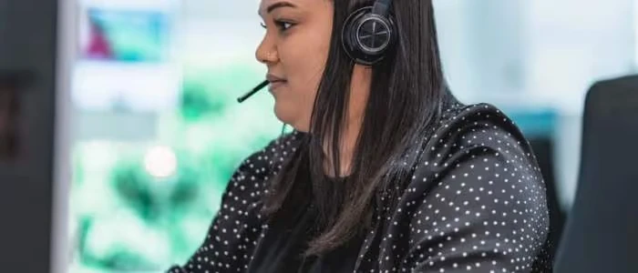 A woman wearing a headset is sitting at a desk, working on a computer.