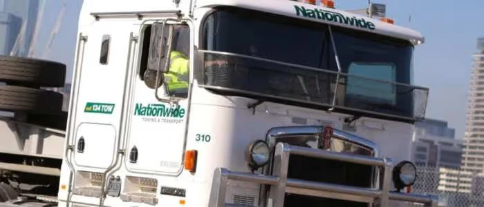 A white tow truck labeled "Nationwide" is towing another vehicle in an urban area.