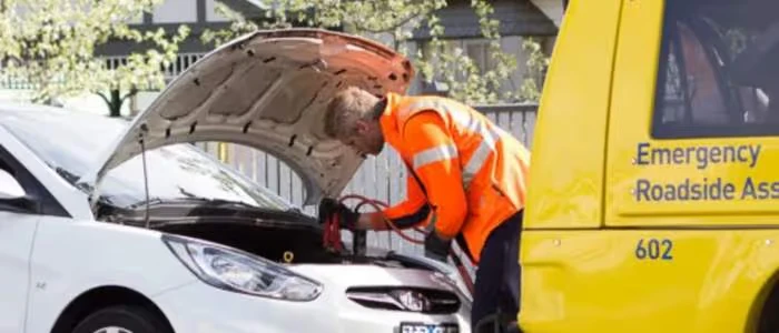 Roadside assistance worker jump-starts a white car with the hood open.