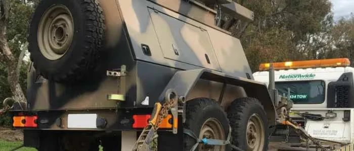 Tow truck transporting a military vehicle securely chained and fastened to the truck.