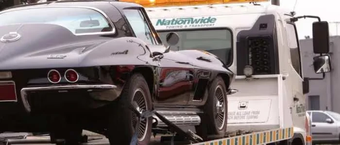 A tow truck is transporting a black vintage car.