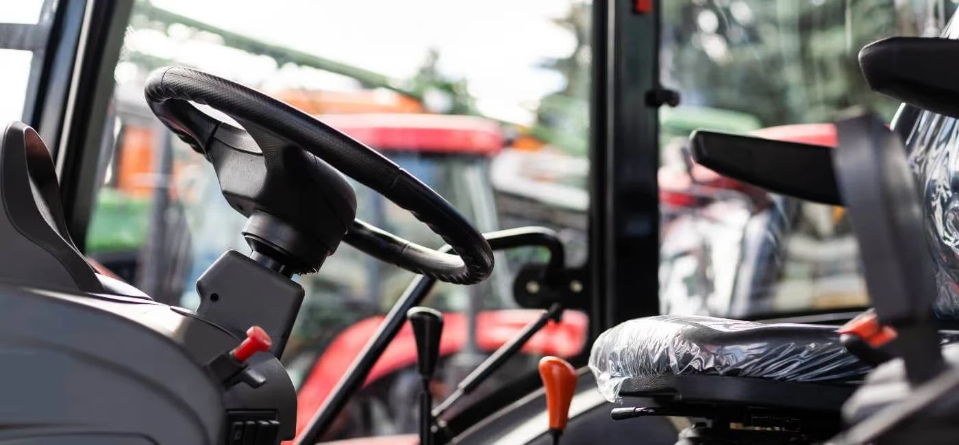 Close-up of a tractor interior showing a steering wheel, control levers, and a plastic-covered seat.