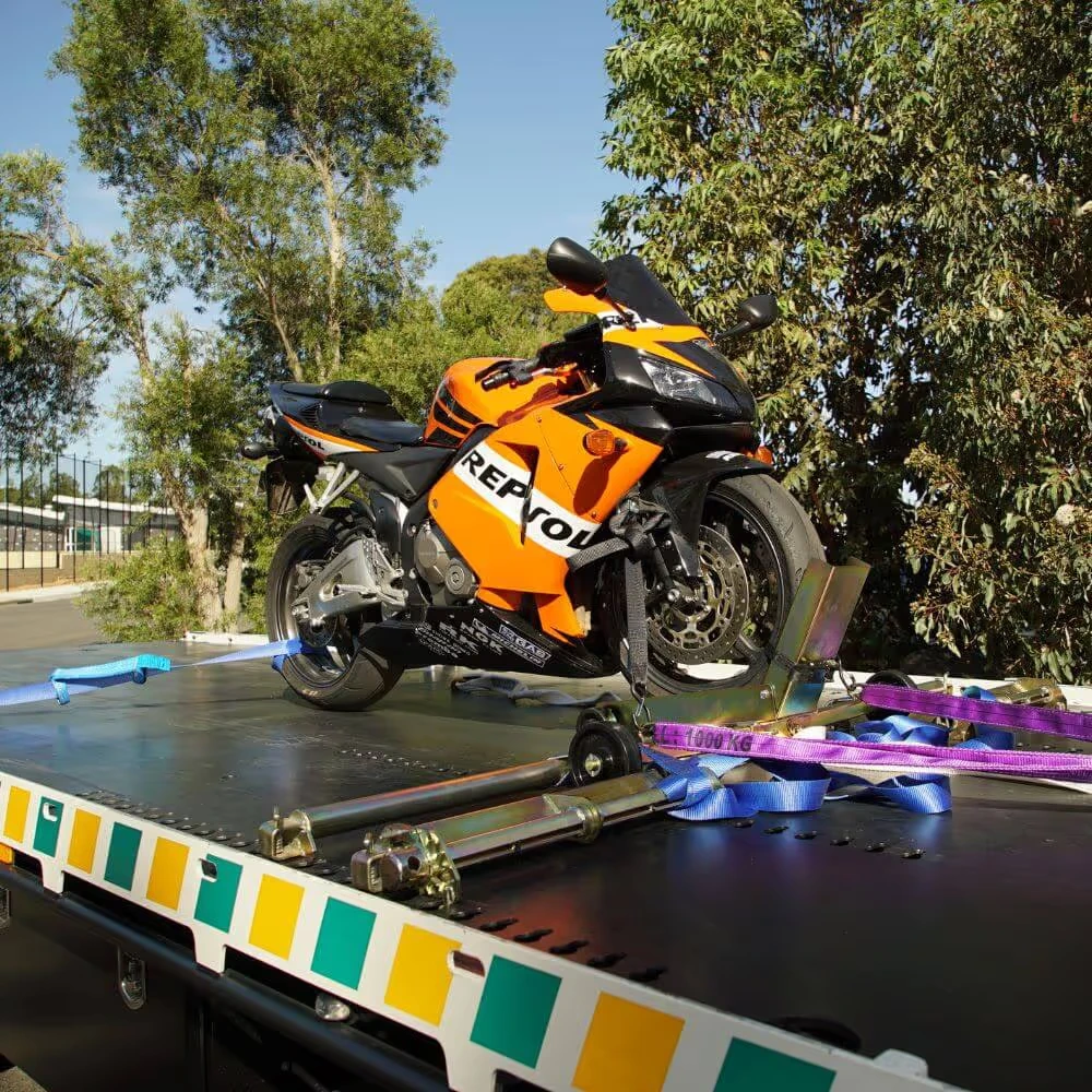 An orange and black motorcycle is secured on a flatbed truck for transport.